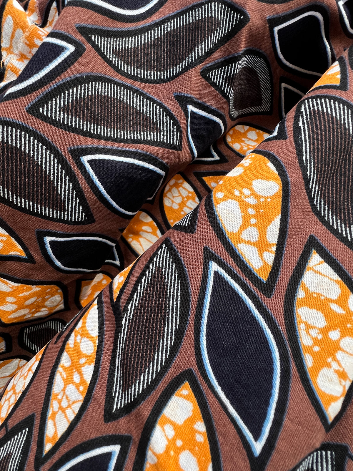 Eweko Cotton Midi Skirt, a tulip-shaped midi skirt in deep navy and orange leaf print Dutch wax cotton on a warm brown background