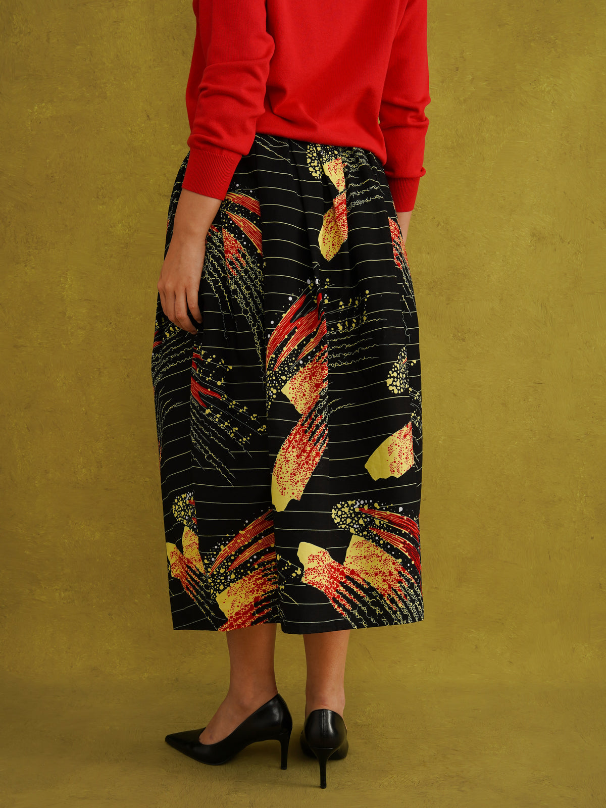 Ariya Cotton Midi Skirt, a tulip-shaped midi skirt in red and yellow Fireworks print Dutch wax cotton on a blue background
