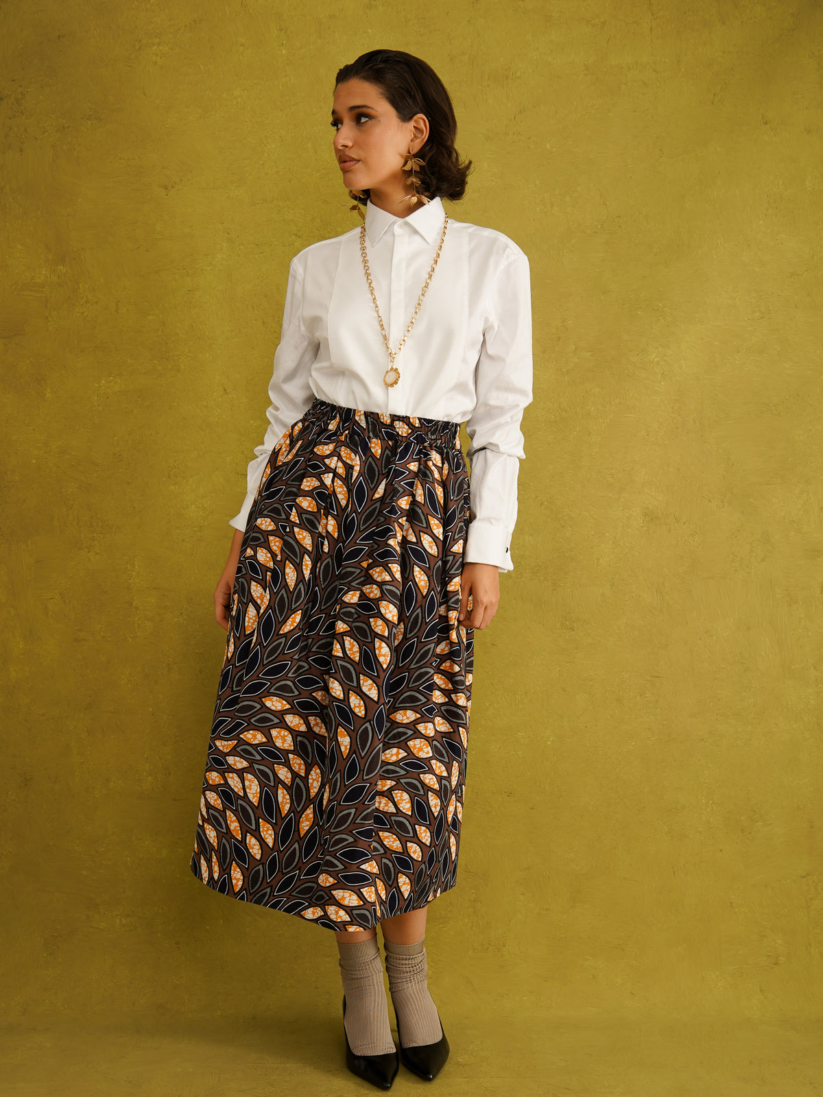 Eweko Cotton Midi Skirt, a tulip-shaped midi skirt in deep navy and orange leaf print Dutch wax cotton on a warm brown background