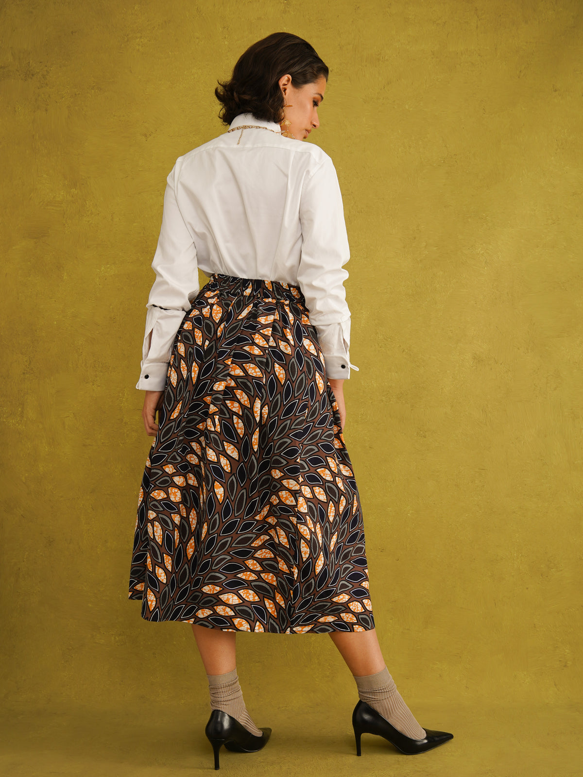 Eweko Cotton Midi Skirt, a tulip-shaped midi skirt in deep navy and orange leaf print Dutch wax cotton on a warm brown background