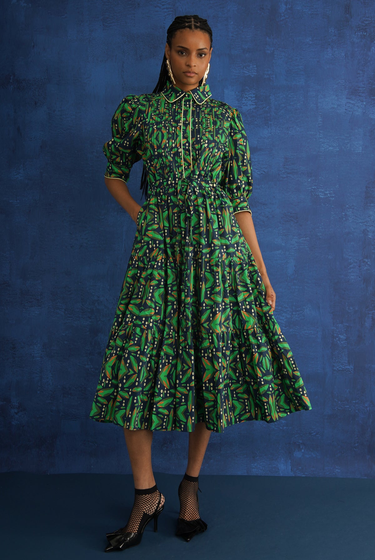 Model wearing The Tomi Cotton Midi Dress in green pintuck print, front view, studio blue background