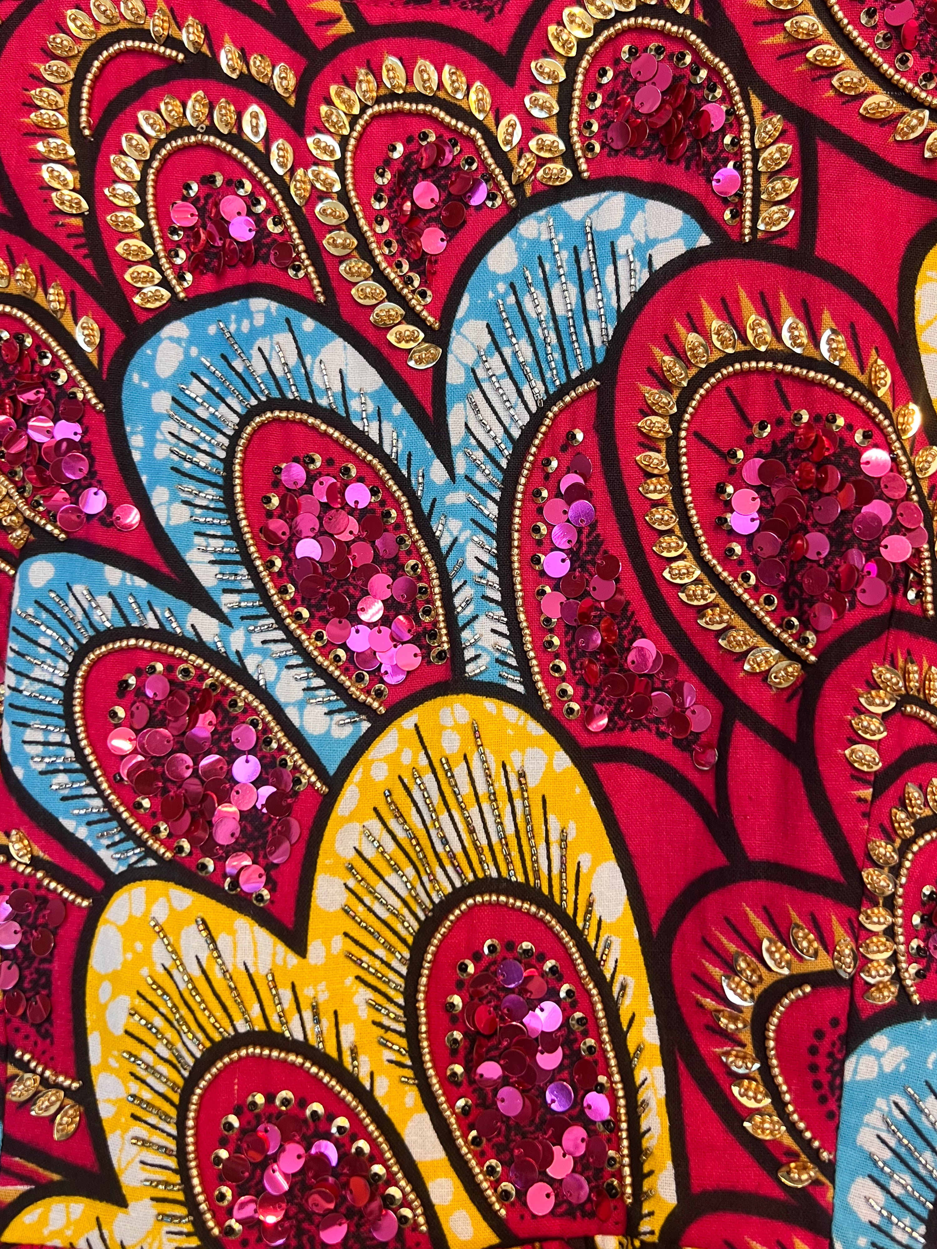 Close-up of hand-beaded detail – sequins and beads in pink and gold on African wax fabric.