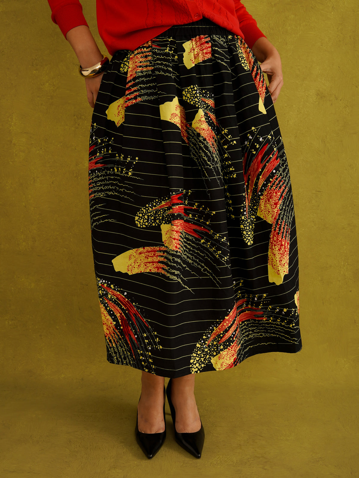 Ariya Cotton Midi Skirt, a tulip-shaped midi skirt in red and yellow Fireworks print Dutch wax cotton on a blue background