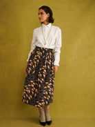 Eweko Cotton Midi Skirt, a tulip-shaped midi skirt in deep navy and orange leaf print Dutch wax cotton on a warm brown background