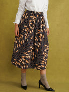 Eweko Cotton Midi Skirt, a tulip-shaped midi skirt in deep navy and orange leaf print Dutch wax cotton on a warm brown background