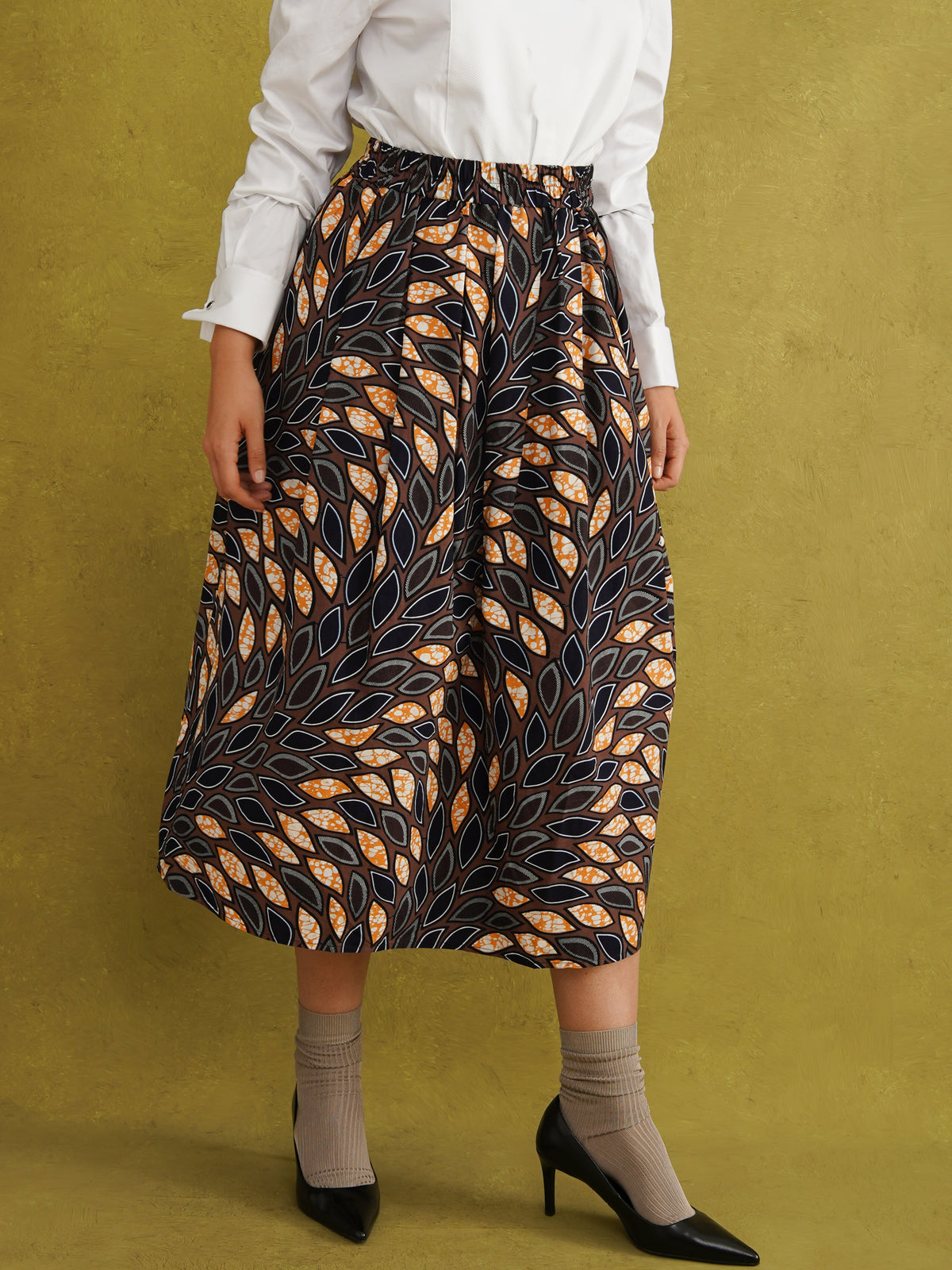 Eweko Cotton Midi Skirt, a tulip-shaped midi skirt in deep navy and orange leaf print Dutch wax cotton on a warm brown background