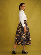 Eweko Cotton Midi Skirt, a tulip-shaped midi skirt in deep navy and orange leaf print Dutch wax cotton on a warm brown background